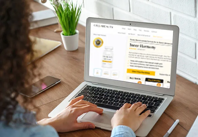 A person uses a laptop displaying a Cellucity website promoting "Inner Harmony" products. The laptop sits on a wooden desk alongside a phone and plant.